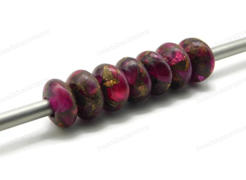 May include: A strand of seven round, pink and gold beads with a metallic sheen. The beads are strung on a silver wire.