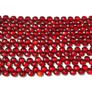 May include: A strand of red gemstone beads, faceted and polished, with a tassel at each end. The beads are arranged in rows, creating a visual pattern.