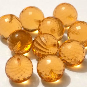 Peut inclure: Un groupe de dix perles de verre facettées de couleur ambre. Les perles sont rondes et ont une finition lisse et polie.