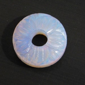 Könnte beinhalten: Ein weißer Opalring mit einem geschnitzten Blumenmuster. Der Ring ist aus einem durchscheinenden Material gefertigt und hat ein Loch in der Mitte.