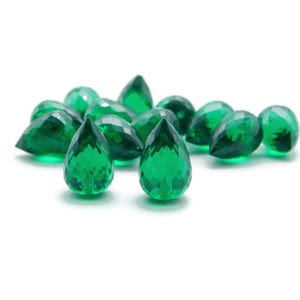 Può includere: Un gruppo di pietre preziose di colore verde smeraldo a forma di pera su uno sfondo bianco.