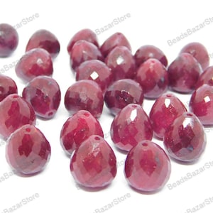 Op de afbeelding: Een verzameling facetgeslepen robijnrode edelsteen kralen. De kralen zijn peervormig en hebben een gladde, gepolijste afwerking.