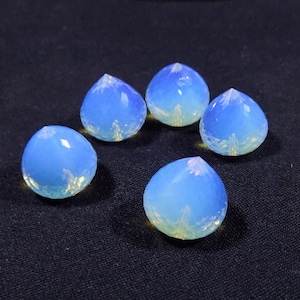 Puede incluir: Cinco piedras iridiscentes de color azul y blanco en forma de lágrima con la parte superior puntiaguda.