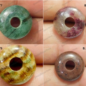 May include: Four round, donut-shaped beads with holes in the center. The beads are made of different types of stone and have unique patterns. The beads are green, purple, brown, and yellow.