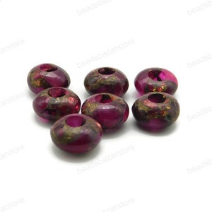May include: A group of eight round, dark pink beads with gold flecks. The beads have a hole in the centre and are made of a translucent material.
