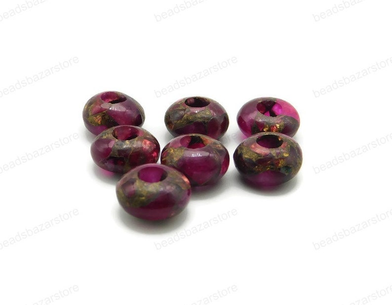 May include: A group of eight round, dark pink beads with gold flecks. The beads have a hole in the centre and are made of a translucent material.