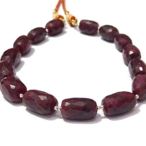 May include: A strand of deep red ruby beads, each bead is faceted and oval shaped. The beads are strung on a silver wire and are separated by small silver spacers.