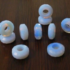 May include: Ten white opal beads with a hole in the center. The beads are faceted and have a slightly iridescent sheen.