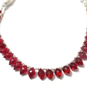 May include: A strand of red gemstone beads with a faceted finish. The beads are strung on a silver chain and are arranged in a graduated pattern, with the largest beads at the bottom.