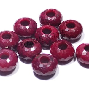 May include: Ten faceted ruby beads with a hole in the center. The beads are a deep red color and are arranged in a loose pile.