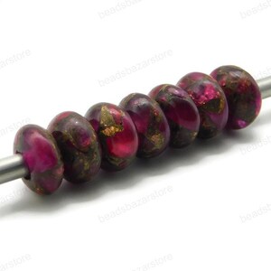 May include: A strand of six round, pink and gold beads with a metallic sheen. The beads are strung on a silver wire.
