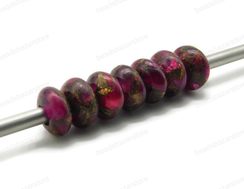 May include: A strand of six round, pink and gold beads with a metallic sheen. The beads are strung on a silver wire.