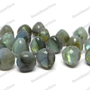 May include: A collection of 17 faceted labradorite gemstone beads in shades of green, blue, and grey. The beads are teardrop shaped and have a pearlescent sheen.