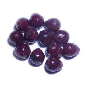 Op de afbeelding: Een groep van 12 facetgeslepen robijn edelsteen kralen in een diepe rode kleur. De kralen zijn traanvormig en liggen los in een hoop.