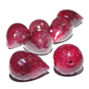 Puede incluir: Un grupo de siete cuentas de rubí facetadas en forma de pera. Las cuentas son de color rojo intenso y tienen un acabado brillante.