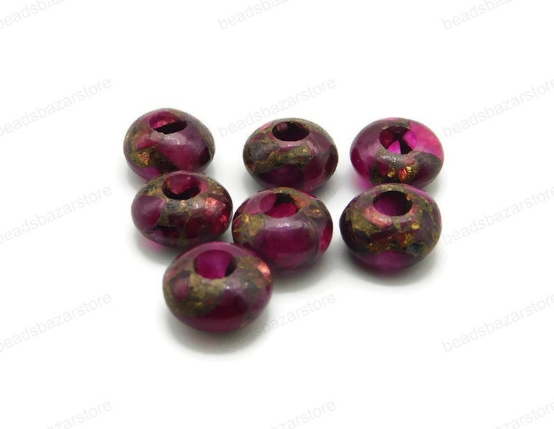 May include: Eight round, pink and gold beads with a hole in the centre. The beads have a speckled, marbled appearance.