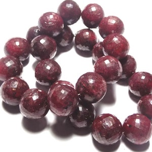 Op de afbeelding: Een streng diepe rode robijn kralen, elke kraal is gefacetteerd en rond, de kralen zijn geregen op een doorzichtige draad.