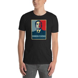 May include: A black t-shirt featuring a red, white and blue graphic of a man's face with the text "Dinkin Flicka" underneath.