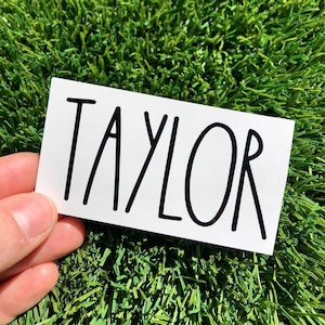 May include: White sticker with the name "TAYLOR" written in black, block lettering.