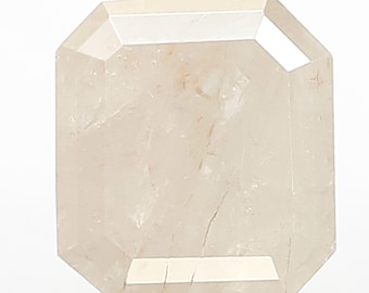 May include: A pale, rectangular gemstone with multiple facets, held by a silver tool. The gem has a slightly translucent appearance, possibly a diamond. The shape is an emerald cut. The gem is held by a pair of tweezers.