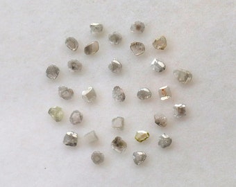 May include: A collection of small, rough, grey diamonds, also known as raw diamonds, arranged in a circle on a white surface.
