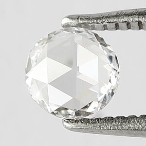 K&ouml;nnte beinhalten: Ein klarer, runder, facettierter Diamant-Edelstein, der von einer Pinzette gehalten wird.