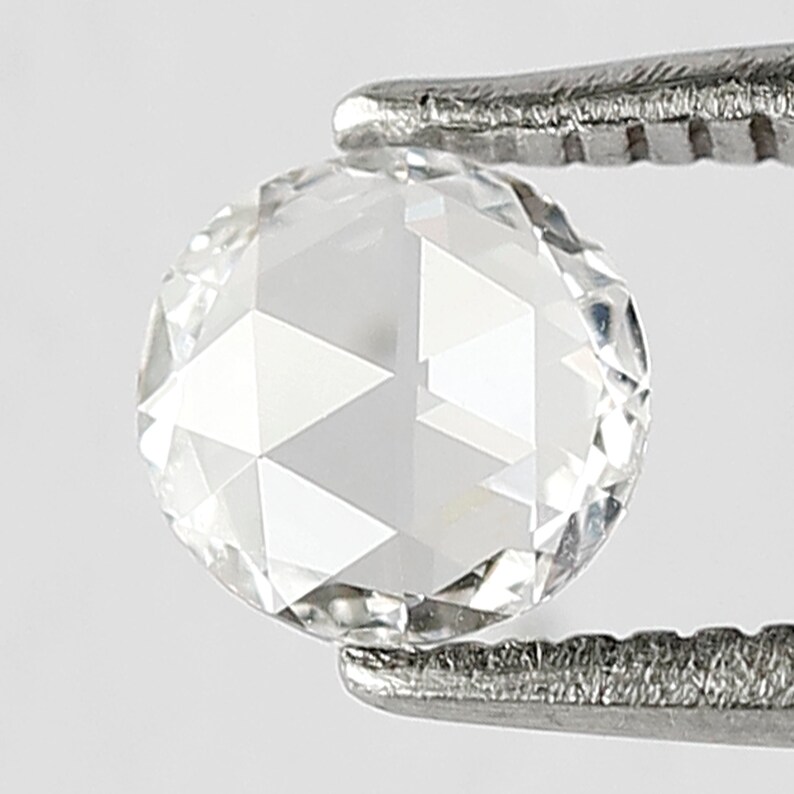 K&ouml;nnte beinhalten: Ein klarer, runder, facettierter Diamant-Edelstein, der von einer Pinzette gehalten wird.