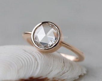 Può includere: Un anello in oro rosa con una pietra preziosa rotonda, trasparente e sfaccettata incastonata in una montatura a castone.