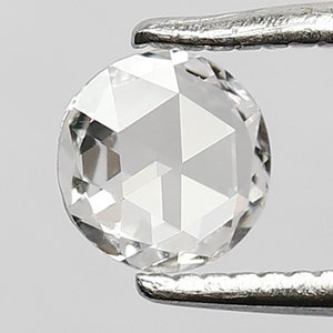 K&ouml;nnte beinhalten: Ein klarer, runder, facettierter Diamant-Edelstein, der von einer Pinzette gehalten wird. Der Diamant hat einen Brillantschliff und ist in einer Zargenfassung gefasst.