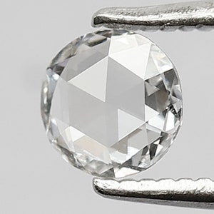 K&ouml;nnte beinhalten: Ein klarer, runder, facettierter Diamant-Edelstein, der in einer Pinzette gehalten wird. Der Diamant hat einen Brillantschliff und ist in einer Zargenfassung gefasst.