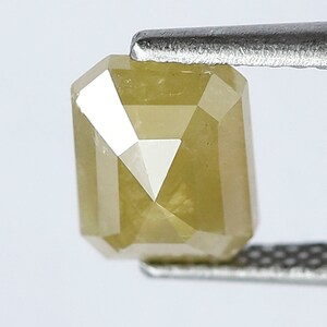 May include: A yellow, faceted, emerald cut diamond gemstone. The diamond is held in a pair of tweezers.