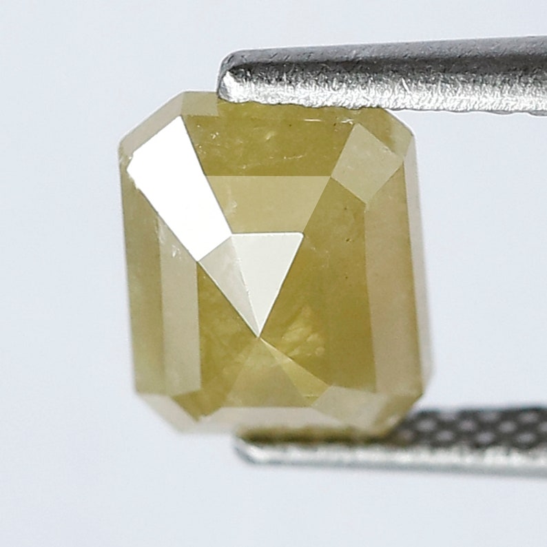 May include: A yellow, faceted, emerald cut diamond gemstone. The diamond is held in a pair of tweezers.