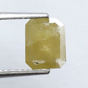 May include: A light yellow, faceted, rectangular diamond gemstone with a rough, natural finish.