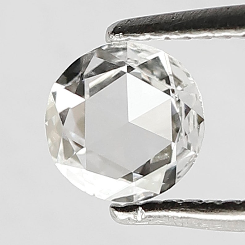 K&ouml;nnte beinhalten: Ein klarer, runder, facettierter Diamant-Edelstein, der von einer Pinzette gehalten wird. Der Diamant ist ein Brillantschliff mit vielen Facetten.