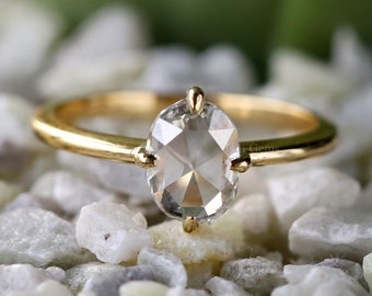 May include: A gold ring with a round, clear, faceted gemstone. The ring is set on a bed of small, white stones.