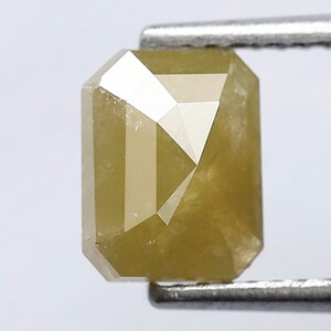 May include: A light yellow emerald cut diamond with a faceted surface.