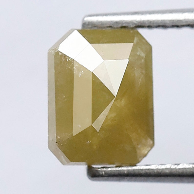 May include: A light yellow emerald cut diamond with a faceted surface.