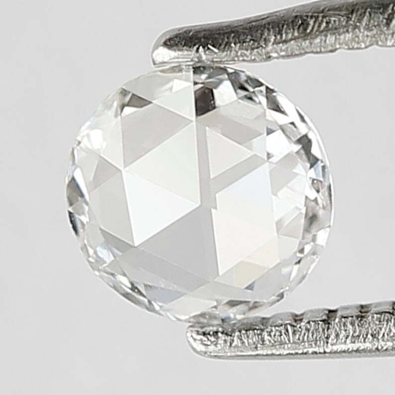 K&ouml;nnte beinhalten: Ein klarer, runder, facettierter Diamant-Edelstein, der in einer Pinzette gehalten wird.