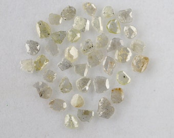 May include: A collection of rough, unpolished diamonds in various sizes and shapes. The diamonds are a pale, greyish-yellow colour and have a natural, raw appearance.