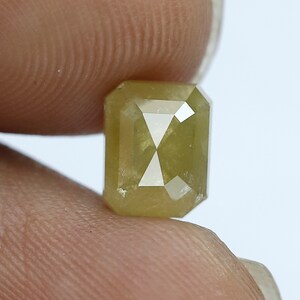 May include: A light green emerald cut rough diamond with a faceted design.