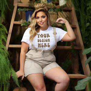 May include: A woman wearing a white t-shirt with the text "YOUR DESIGN HERE" in brown, paired with khaki shorts and suspenders. She is sitting on a wooden ladder with greenery in the background.