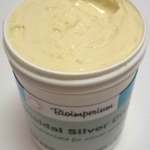 Pode incluir: Um frasco de plástico branco com um rótulo azul e branco. O rótulo diz "Bioimperium Colloidal Silver Cream Guaranteed for Silver Purity 4 ounces". O frasco está cheio de um creme amarelo claro.