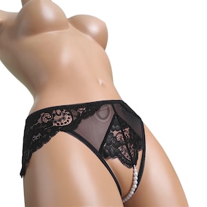 May include: Black lace and sheer mesh knickers featuring a high-cut leg design, a triangular lace panel at the centre front, and a vertical string of white faux pearls connecting the waistband to the crotch area on a mannequin.
