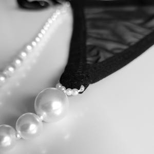 Könnte beinhalten: Ein schwarzes Netzgewand mit Perlenbesatz und einer daran befestigten Perlenkette.