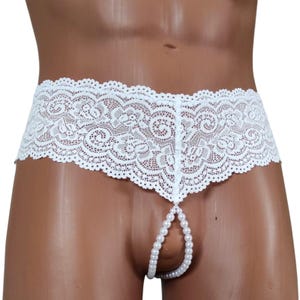 Op de afbeelding: Witte kanten onderbroek met een geschulpte rand en een parelketting. Het ondergoed heeft een bloemen kanten patroon en een laag model. De parelketting hangt naar beneden vanaf de voorkant van het ondergoed.