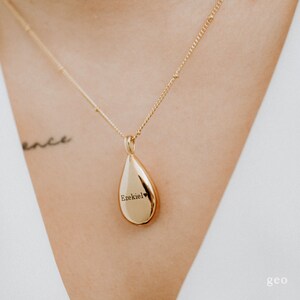 May include: Gold teardrop necklace with the name "Ezekiel" engraved on the pendant.