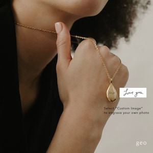 May include: A gold teardrop-shaped pendant necklace with a delicate chain. The pendant has the words "Love you" engraved on it. The necklace is being held by a person's hand.