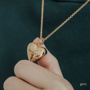 May include: Gold heart-shaped pendant necklace with the inscription "Matthew 5" hanging from a gold chain.