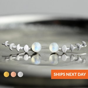 May include: A pair of silver moon phase earrings with moonstone beads. The earrings are made of sterling silver and feature a crescent moon design.