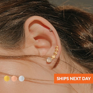 May include: Gold crescent moon earrings with a small round gemstone earring. The earrings are shown in a person's ear.